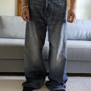 Weekday Astro Loose Baggy Jeans blå - Säljer ett par Weekday Astro Loose Baggy Jeans i klassisk blå tvätt. De har riktigt bred passform och baggy stil, med slitningar och ljusa partier för en cool, avslappnad look. Jeansen är tillverkade i bomull och har fem fickor och dragkedjegylf. W30 L34