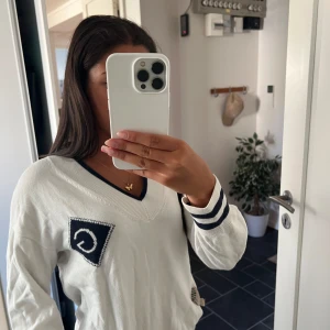 Vit v-ringad tröja från GANT - Säljer en vit v-ringad tröja från GANT med marinblå detaljer vid halsringning och ärmslut. Tröjan har ett broderat GANT-märke på bröstet och är långärmad. Perfekt för en preppy look och passar snyggt till jeans.