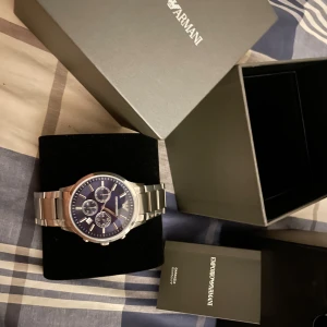 Emporio Armani blå klocka i stål - Stilren klocka från Emporio Armani med blå urtavla och silverfärgade detaljer. Klockan har tre mindre urtavlor, datumvisning och en robust länk i rostfritt stål. Perfekt accessoar för dig som gillar klassisk och modern design.