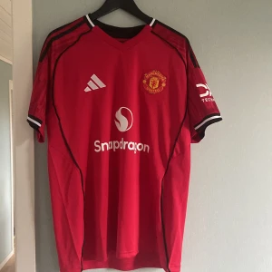 Manchester United Bruno Fernandes - Manchester Uniteds officiella matchtröja från Adidas med B. Fernandes och nummer 8 på ryggen. Säsongen 25/26 hemmaställ