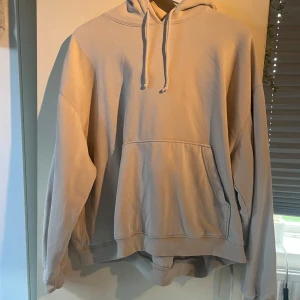 Beige hoodie från Weekday i storlek L - Oversized beige hoodie från Weekday med huva och snörning. Tröjan har en stor magficka och långa ärmar. Mjuk insida och klassisk passform. Enkel och stilren design utan tryck eller mönster. Frakt tillkommer