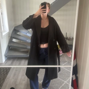Lång svart kappa från Nelly - Säljer en svart lång kappa med bälte i midjan och stora slag. Kappan har knappar framtill och vid ärmsluten, samt en klassisk rak passform. Har även en slits bak som ni kan se på ena bilden☺️ Hund finns i hemmet så förekommer ett och annat hundhår🙈 den är i bra skick och jag är 177 till referens🥰 kom med prisförslag om priset inte passar😊