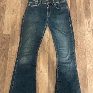 Mörkblå low flare jeans - Snygga mörkblå jeans med låg midja och flare-ben. Klassisk femficksmodell med slitningar för en cool look. Jeansen har dragkedja och knapp framtill och är tillverkade i ett robust denimtyg. Är avända men i fint skick😊