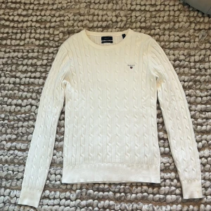 Vit kabelstickad tröja från Gant - Kabelstickad vit tröja från Gant med rund halsringning och broderad logga på bröstet. Långärmad och i klassisk, tidlös design som är enkel att matcha. Perfekt för dig som gillar stilrent. Pris kan diskuteras!