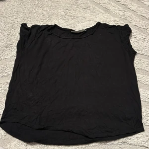 Svart enkel topp i bomull - En basic svart topp med rund hals och korta ärmar. Tillverkad i mjuk bomull, perfekt för en avslappnad och stilren look. Passar till allt och är lätt att matcha med andra plagg.