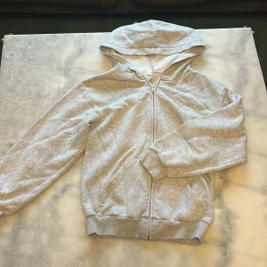 Grå hoodie med dragkedja från H&M - Enkel och stilren ljusgrå hoodie från H&M i storlek 134/140. Tillverkad i mjuk bomullsmix, perfekt för chill dagar. Har lite lila fläckar på sig!!💞