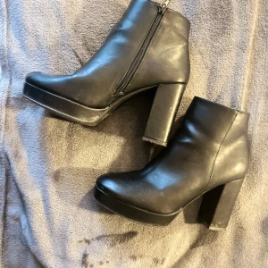 Svarta boots med klack och dragkedja - Snygga svarta boots  i storlek 39. Skorna har hög klack, plattform och dragkedja på sidan. Tillverkade i syntetmaterial med rund tå och stilren design som passar till många outfits.