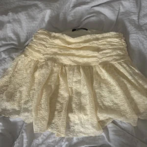 Gul spetskjol från Gina Tricot - Supersöt ljusgul kortkjol från Gina Tricot med volangig form och bred smock i midjan. Kjolen har ett lager av blommig spets och är fodrad under. Perfekt för dig som vill ha en romantisk och feminin vibe till din outfit. Kjolen är endast använd 1-2 gånger