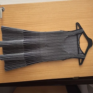 Randig ärmlös kortklänning - Snygg ärmlös kortklänning med svart och vit randigt mönster. Klänningen har rundad urringning och lätt utställd kjol, perfekt för en trendig och avslappnad look. Materialet känns mjukt och följsamt mot kroppen.