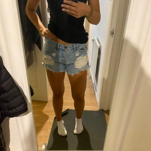 Ljusa jeansshorts från Topshop - Snygga ljusblå jeansshorts från Topshop med slitna detaljer och fransig kant. Klassisk femficksmodell med låg midja och dragkedja. Perfekta för sommaren och ger en avslappnad vibe.
