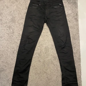 Svarta Replay Grover Hyperflex jeans - Säljer ett par svarta Replay Grover Hyperflex jeans i straight fit. Byxorna har klassisk femficksdesign, snygga svarta sömmar och är tillverkade i ett stretchigt material som ger extra komfort. Perfekta för dig som gillar stilrena och bekväma jeans. Liten repa syns i på sista bilden.