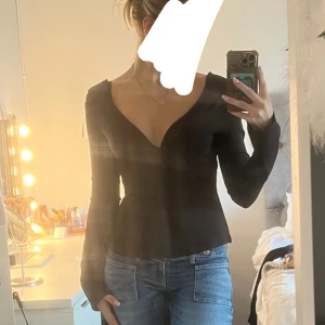 Svart långärmad topp med öppen rygg - Säljer en svart långärmad topp med djup v-ringning framtill och öppen rygg med snygg knyt-detalj. Från Nelly helt ny aldrig använd