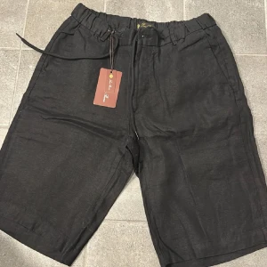 Svarta linneshorts från Loro Piana - Svarta shorts från Loro Piana i 100% linne med elastisk midja och snörning. Klassisk och stilren design med diskreta fickor och en liten logodetalj bak. Perfekta för varma dagar när du vill ha en clean och chill look.