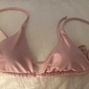 Ljusrosa trekantsbikini - Säljer en ljusrosa trekantsbikini med smala axelband och knyt i ryggen. Enkel och stilren design som ger en fräsch look på stranden. Perfekt för dig som gillar minimalistiska badkläder.