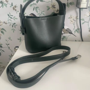 Mörkgrön liten väska - En liten väska från Rizzo i en mörkgrön färg! Aldrig använd så den är i väldigt fint skick :) Ca. 15 cm hög om man inte räknar med handtaget och ca. 18 cm bred.