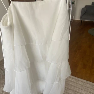 Vit studentklänning, stl 36 - Superfin vit kjol i organza med flera lager volanger och elastisk midja med knytband. Kjolen har en luftig och flowy känsla, perfekt för dig som vill ha en romantisk och trendig look. Passar snyggt till crop tops eller stickade tröjor eller student 