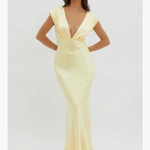 champange långklänning med öppen rygg - Supersnygg långklänning i satin-look med djup v-ringning och korta ärmar. Klänningen har en öppen rygg med twistad detalj och figurnära passform som ger en elegant siluett. Färgen är lite mer champangefärgad än vad bilderna visar men klänningen sitter verkligen så fint på kroppen