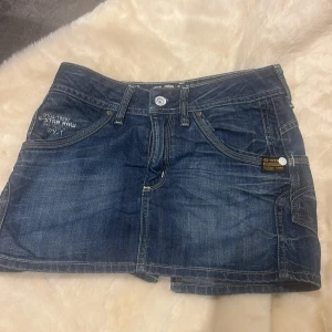 Jeanskjol vintage stl 25 - Snygg blå jeanskjol från G-Star RAW med klassiska fickor fram och bak, coola kontrastsömmar och detaljer som bälteshällor och logopatch. Perfekt för dig som gillar streetstyle och vill ha en kort, tidlös denimlook.