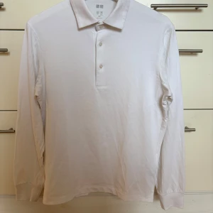 Vit långärmad pikétröja Uniqlo Airism storlek XXS - Vit långärmad pikétröja från Uniqlo Airism i mjuk bomulls- och polyestermix. Klassisk krage, tre knappar framtill och ribbade muddar vid ärmslut. Perfekt att träna i! Storlek XXS