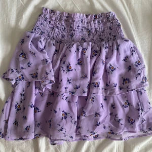 Ljuslila blommig volangkjol Madawool - Säljer en jättesöt kjol som jag sytt själv för några år sen. Använd några fåtal gånger. Den är lilla med små blommor på. Skulle säga att storleken är S men är stretchig i midjan så passar upp till M/L