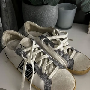 Karl Lagerfeld vita sneakers med silverdetaljer - Snygga vita sneakers från Karl Lagerfeld med glittriga silverdetaljer på häl och snörning. Skorna har svart logotyp på sidan, vita skosnören och beige sula. Perfekta för dig som vill sticka ut med en cool och trendig look. Köpta secondhand men aldrig använda sen dess. Orginalpris 1200kr🥰🥰💗