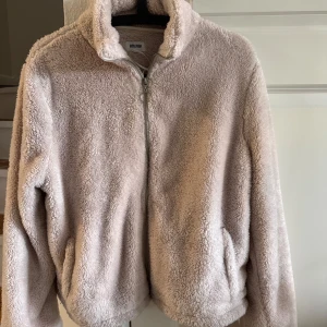 Beige teddyjacka från Bubbleroom - Supermjuk och fluffig teddyjacka från Bubbleroom i beige. Jackan har hög krage, dragkedja framtill och två fickor. Perfekt för kyliga dagar när du vill vara både varm och snygg. Oversized fit för en chill vibe.