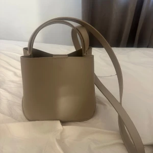 Beige axelväska - Snygg beige väska från Gina tricot. Inuti finns en praktisk dragkedja för säker förvaring av dina saker.