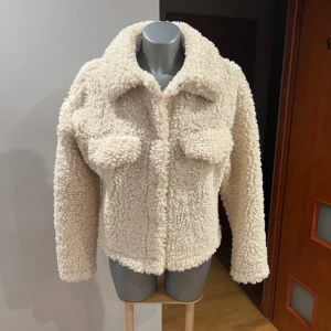 Beige teddyjacka - Mysig beige teddyjacka med långa ärmar och en klassisk krage. Jackan har en fluffig textur och stängs med knappar framtill. Perfekt vår jacka! 😍