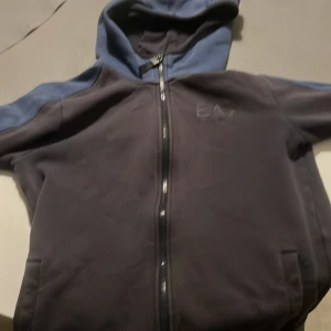 Mörkblå hoodie från Emporio Armani pris kan diskuteras  - Säljer en snygg mörkblå hoodie från Emporio Armani med dragkedja och huva. Den har en stilren design med EA7-logga på bröstet och är perfekt för en avslappnad stil. Passar bra för kyligare dagar.