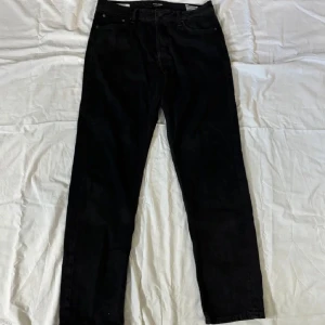 Svarta jeans från Jack & Jones - Säljer ett par svarta jeans från Jack & Jones i loose fit. De har en klassisk design med fem fickor och knappar i midjan. Perfekta för en avslappnad stil. De är i nyskick och är i storlek: W30 L32. Modellen är ”Loose/Chris. Vid fler frågor är det bara att slå ett pling i dm!☺️