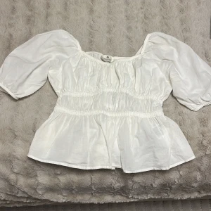 Vit blus från H&M - Säljer en söt vit blus från H&M med puffiga ärmar och elastiska detaljer som ger en fin passform. Den är genomskinlig och har små fläck. 