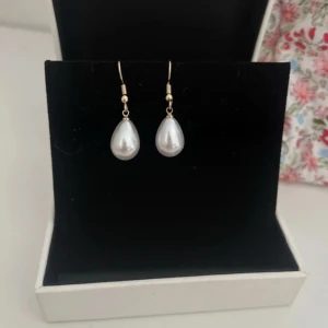 Örhängen med vita pärlor - Eleganta örhängen med droppformade vita pärlor. Perfekta för att ge en klassisk touch till din outfit. Hängs på örat med en enkel krok.