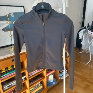 Träningsjacka - Snygg grå jacka från H&M Move i ett mjukt och stretchigt material. Jackan har en dragkedja framtill och långa ärmar, perfekt för en aktiv livsstil. Tillverkad av polyester och elastan för en bekväm passform.