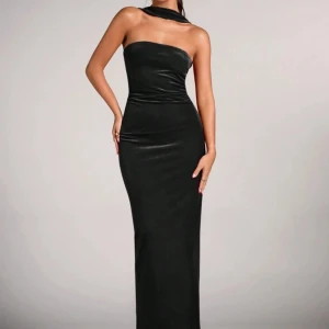 Svart axelbandslös långklänning - Elegant svart långklänning med en axelbandslös design och öppen rygg. Klänningen har en tight passform som framhäver figuren och är perfekt för festliga tillfällen.