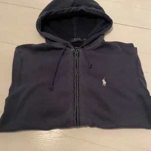 Mörkblå hoodie från Ralph Lauren - Säljer en snygg mörkblå zip hoodie från Ralph Lauren då jag inte använder den så mycket. Den är köpt på NK för 1600kr och kvitto finns. Tveka inte på att skriva om du har frågor