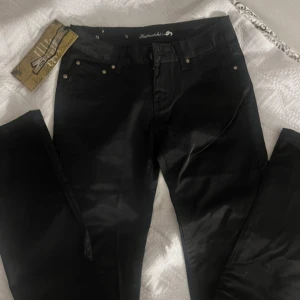 Svarta skin jeans från Kaiweishi - Snygga svarta jeans från Kaiweishi med en slim passform. De har en klassisk design med fem fickor och knappar i silverfärg. Perfekta för en stilren look.