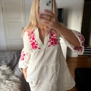 Vit klänning med rosa broderi - Super gullig vit klänning med v-ringad hals och rosa broderade blommor på bröstet och ärmarna. Helt ny!!!