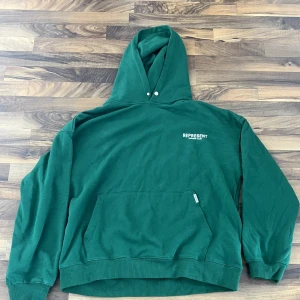 Grön hoodie från Represent - Säljer en grön hoodie från Represent med tryck på både fram- och baksidan. Den har en klassisk känguruficka och justerbar huva med dragsko. Perfekt för en avslappnad stil. 