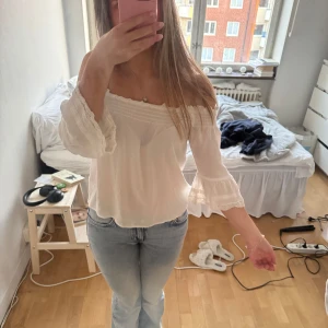Vit offshoulder blus med spetsdetaljer - Säljer en söt vit offshoulder blus med spetsdetaljer vid ärmslut. Blusen har en luftig passform och utsvängda trekvartsärmar med brodyr. Perfekt för varmare dagar, passar till både jeans och kjol! Egentligen barnstorlek men passar xs