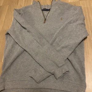 Grå tröja från Ralph Lauren - Säljer en stilren grå tröja från Ralph Lauren med dragkedja vid halsen. Tröjan har långa ärmar och en liten broderad logotyp på bröstet. Perfekt för en avslappnad och snygg look.