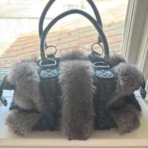 Handväska med pälsdetaljer - Super snygg mörkblå handväska med grå fuskpäls detaljer! Med glittrigt flätat tyg och flätade handtag. Väskan är stor och rymlig, med två små innerfack och ett stort med dragkedja! Köpte second hand och använt ett fåtal gånger, väldigt bra skick! 💕