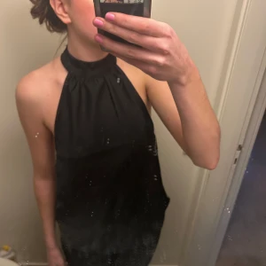 Svart halterneck topp - Snygg svart topp med halterneck-design och öppen rygg. Perfekt för en elegant kvällslook. Använt en gång, någorlunda liten i storlek, skulle kunna vara S.