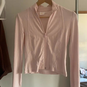 Ljusrosa tränings tröja med dragkedja - Säljer en ljusrosa tränings tröja med dragkedja framtill. Tröjan har långa ärmar och en stilren design. Har lite ”hål” men var så när jag köpte den, kan finnas några svaga fläckar på