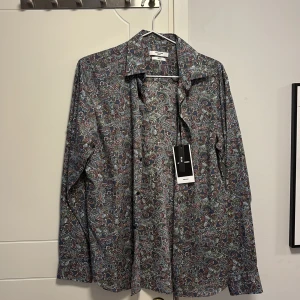 Mönstrad skjorta från Jack & Jones - Snygg mönstrad skjorta från Jack & Jones i en mix av blå, röd och grön. Skjortan har en slim passform och långa ärmar, perfekt för en stilren look. Tillverkad i ett mjukt material med knappar framtill.