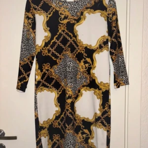 Mönstrad klänning från Sisters Point - Ej använd. Snygg klänning från Sisters Point med ett iögonfallande mönster i svart, guld och leopard. Klänningen har trekvartsärmar och en elegant passform som passar perfekt för en kväll ute. Materialet är mjukt och bekvämt.