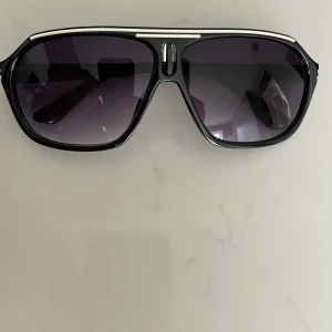 Svarta solglasögon med silverdetaljer - Snygga svarta solglasögon med en klassisk design och silverdetaljer på bågarna. Glasen är mörka och ger ett stilrent intryck. Perfekta för soliga dagar och en cool look.