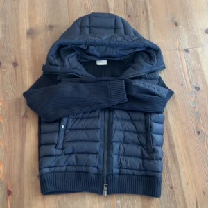 Moncler trickot  - Säljer en snygg mörkblå dunjacka från Moncler med huva och dragkedja. Jackan har ribbade ärmar och nederkant för extra komfort. Perfekt för kyliga dagar när du vill hålla stilen. 🧥