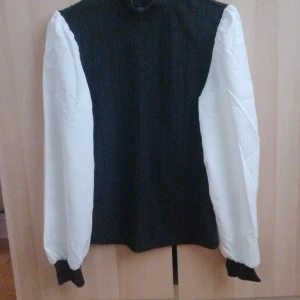 Svart och vit tröja från Shein - Säljer en stilren svart tröja med vita ärmar från Shein. Tröjan har en ribbad struktur och långa ärmar med svarta muddar. Perfekt för en trendig look!