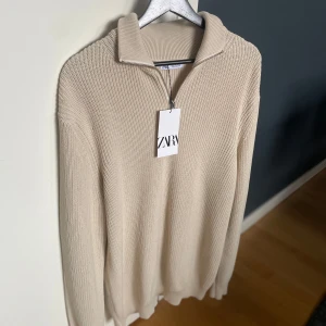 Beige stickad tröja från Zara - Säljer en stilren oanvänd beige stickad tröja från Zara med dragkedja och krage. Perfekt för kyligare dagar med sin mjuka och bekväma passform. Storleken är L-XL, passar 190+ med lite bredare axlar då den är ganska stor i passformen.