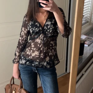 Svart blommig blus - Säljer en svart blommig blus med v-ringning och trekvartsärmar. Blusen har ett transparent material med ett fint blommönster i vitt💗🌟✨